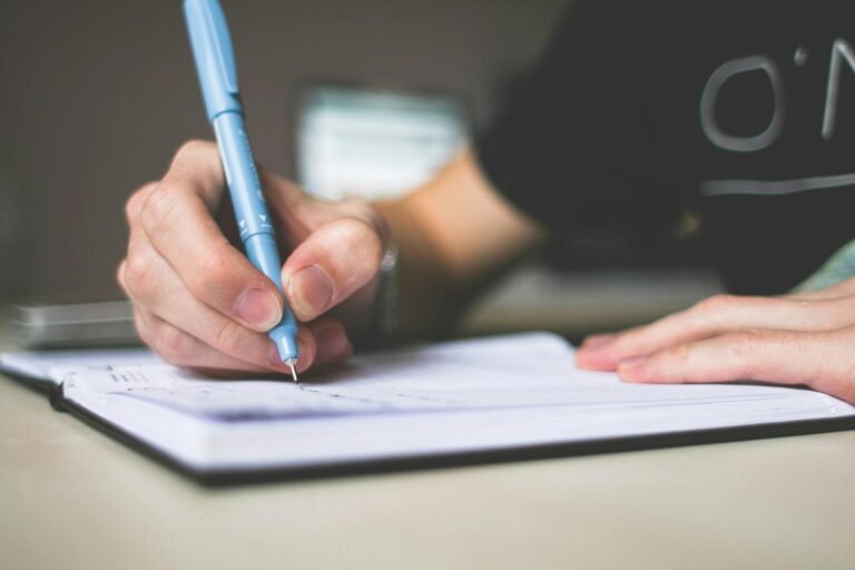 Skrivning Person Holding Blue Ballpoint Pen Writing in Notebook