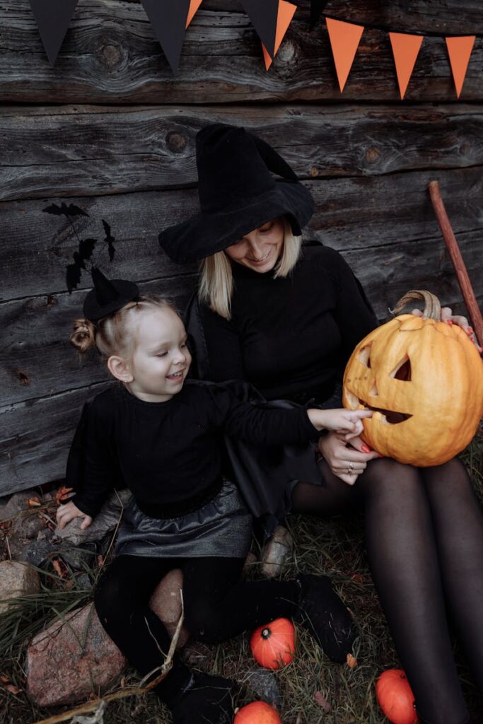 Halloween i Danmark: historie, fejring og spørgsmål besvaret 2 Mother and daughter enjoying Halloween outdoors with a carved pumpkin and costumes by a wooden wall.